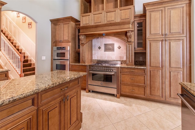 kitchen featuring tasteful backsplash, light stone counters, appliances with stainless steel finishes, light tile patterned floors, and custom exhaust hood