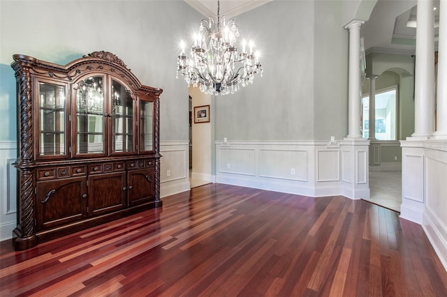 unfurnished dining area with ornate columns, crown molding, dark hardwood / wood-style floors, and an inviting chandelier