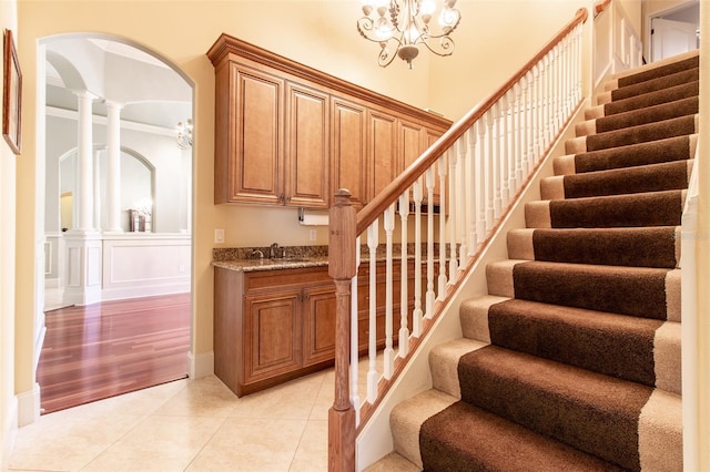 stairway featuring tile patterned floors, ornate columns, crown molding, sink, and a chandelier