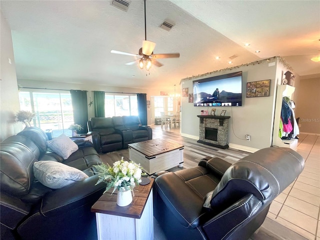 living room featuring ceiling fan, a stone fireplace, hardwood / wood-style floors, a textured ceiling, and lofted ceiling