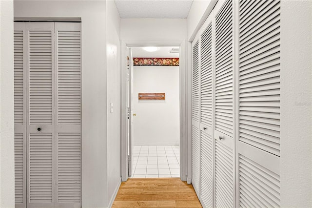 hall with a textured ceiling and light wood-type flooring