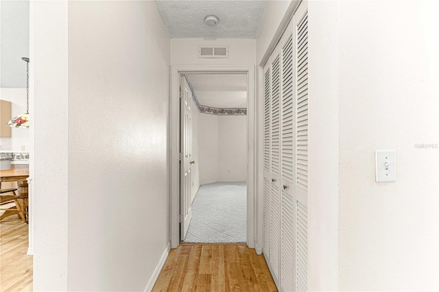 hallway with a textured ceiling and light hardwood / wood-style flooring