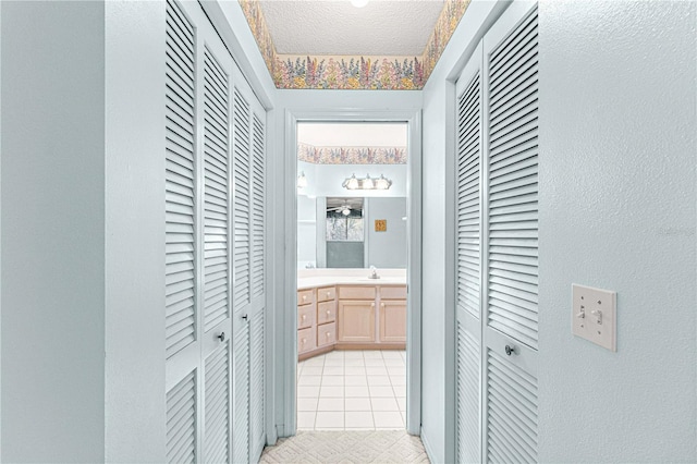 corridor with a textured ceiling, light tile patterned floors, and sink