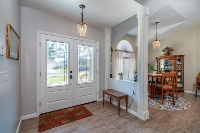 foyer with decorative columns, french doors, a chandelier, and light wood-type flooring