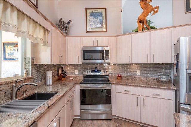 kitchen featuring appliances with stainless steel finishes, light hardwood / wood-style flooring, tasteful backsplash, light stone counters, and light brown cabinetry