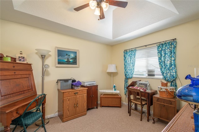 carpeted home office with ceiling fan and a tray ceiling