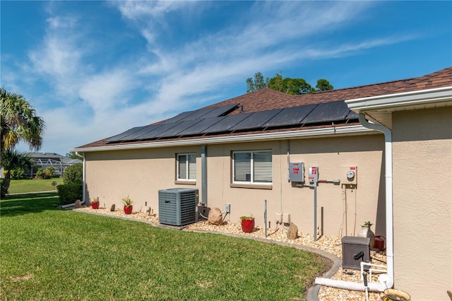 rear view of house with solar panels, a yard, and central air condition unit