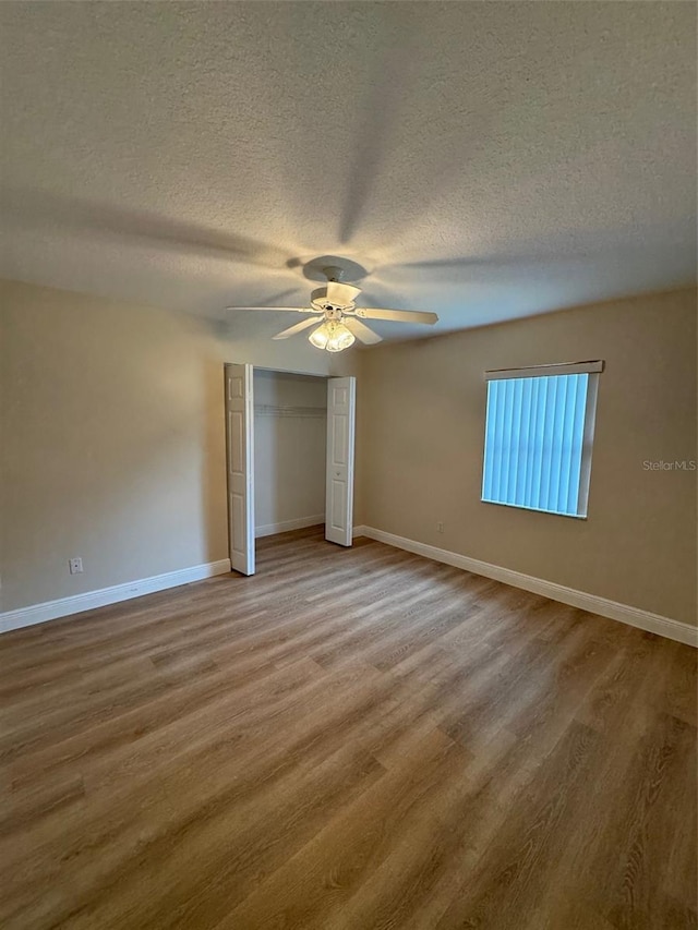 unfurnished bedroom with a textured ceiling, ceiling fan, wood-type flooring, and a closet