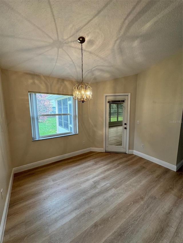 unfurnished dining area with a chandelier, a textured ceiling, wood-type flooring, and a wealth of natural light