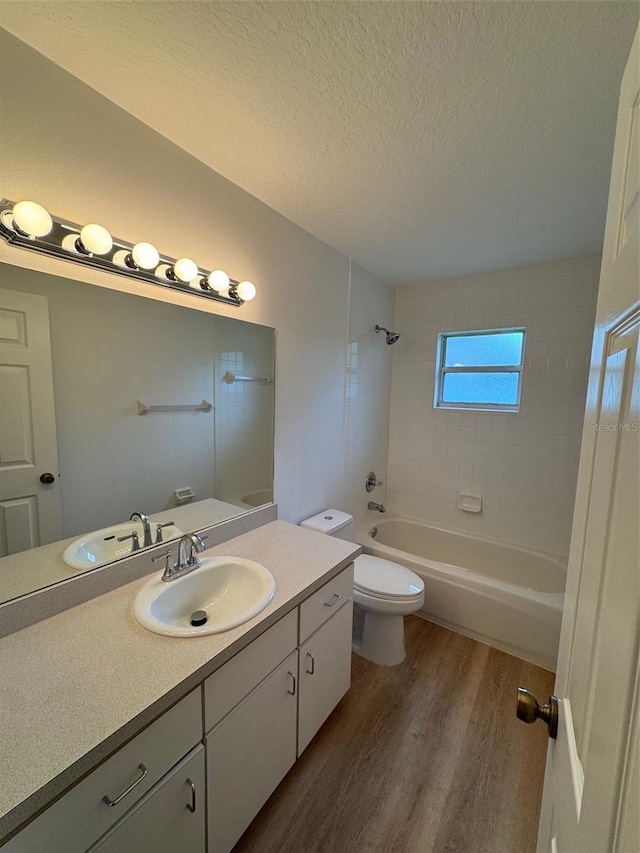 full bathroom featuring a textured ceiling, toilet, vanity, tiled shower / bath combo, and wood-type flooring