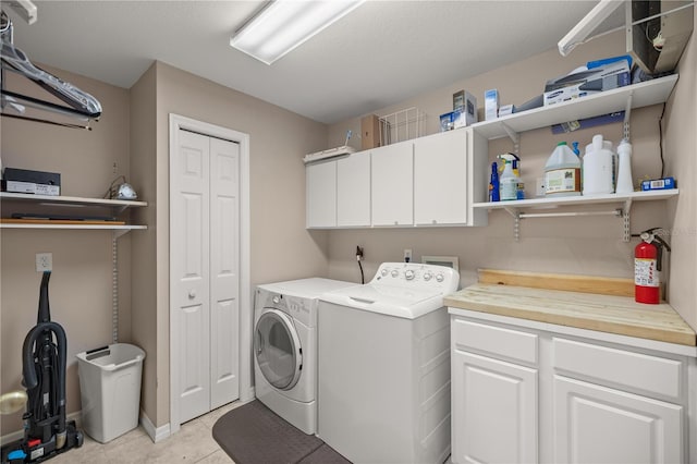 clothes washing area with cabinets, light tile patterned flooring, and washing machine and clothes dryer