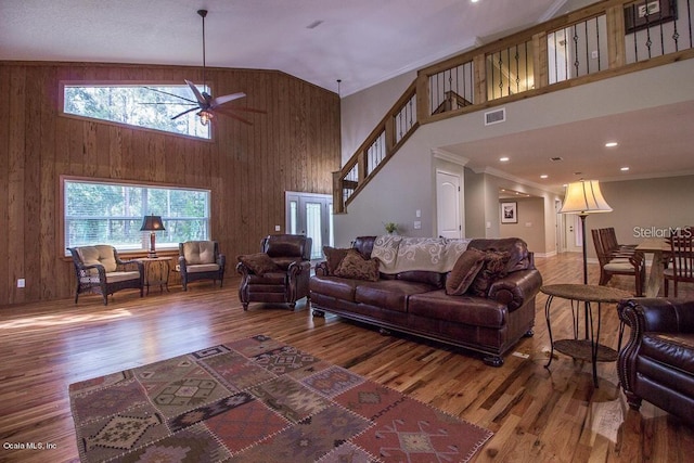 living room featuring wood walls, ceiling fan, ornamental molding, a towering ceiling, and wood-type flooring