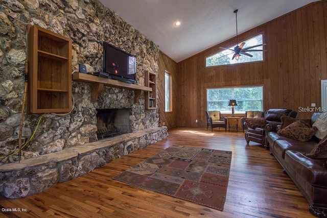 living room featuring ceiling fan, wood walls, a textured ceiling, a fireplace, and hardwood / wood-style flooring