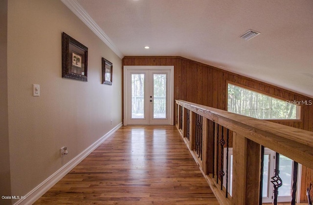 hall with wood walls, french doors, wood-type flooring, and ornamental molding