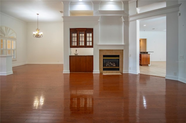 unfurnished living room with ornamental molding, wood-type flooring, an inviting chandelier, and a tiled fireplace