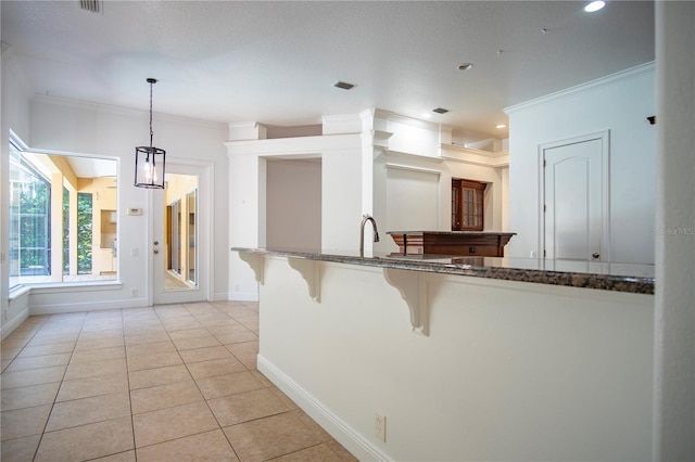 kitchen with light tile floors, a kitchen bar, dark stone counters, ornamental molding, and pendant lighting