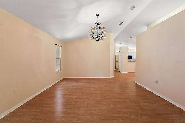 empty room featuring hardwood / wood-style floors, a notable chandelier, and lofted ceiling