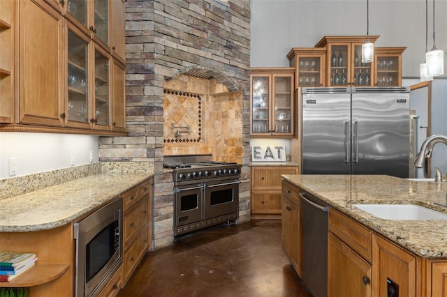 kitchen with built in appliances, sink, light stone countertops, and decorative light fixtures