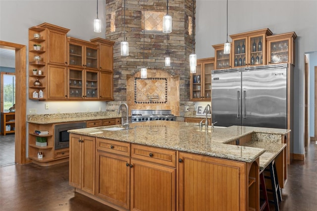 kitchen featuring decorative light fixtures, a high ceiling, a kitchen island with sink, and built in appliances