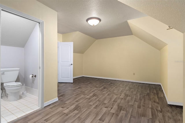 additional living space featuring vaulted ceiling, tile floors, and a textured ceiling