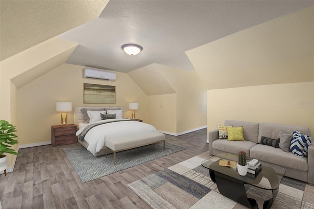 bedroom featuring wood-type flooring, a textured ceiling, vaulted ceiling, and a wall unit AC