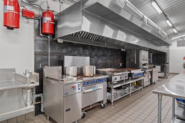 kitchen with stainless steel counters, wall chimney range hood, and light tile floors