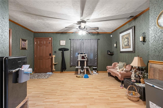 interior space featuring ceiling fan, crown molding, light wood-type flooring, and a textured ceiling