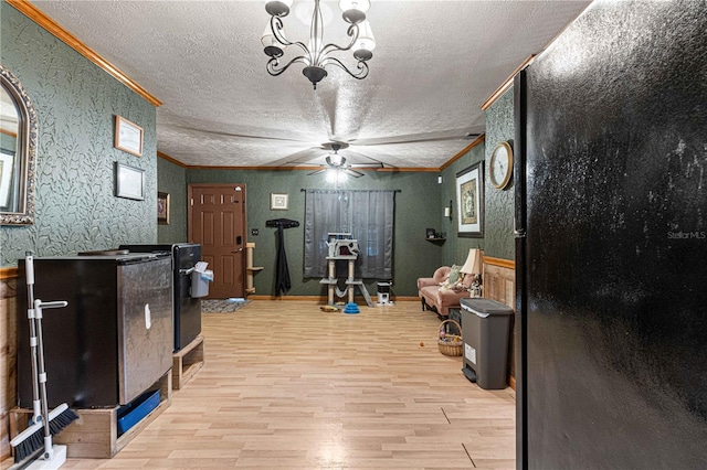 exercise area with ceiling fan with notable chandelier, a textured ceiling, light wood-type flooring, and ornamental molding