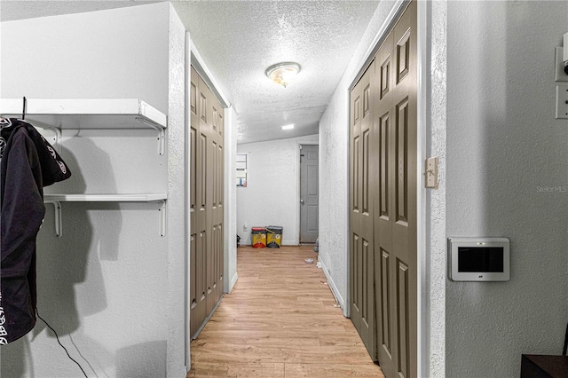 hallway with lofted ceiling, light hardwood / wood-style floors, and a textured ceiling