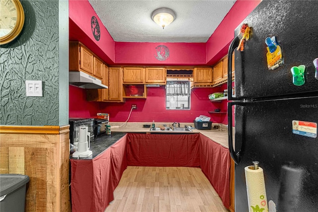 kitchen featuring black refrigerator, light hardwood / wood-style flooring, a textured ceiling, and sink