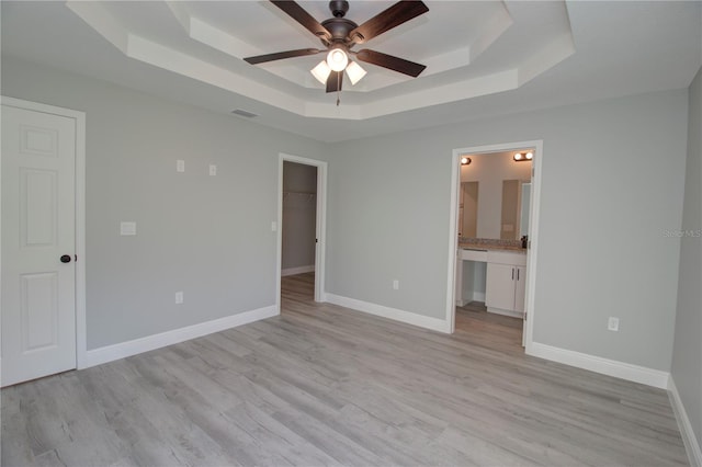 unfurnished bedroom featuring light hardwood / wood-style flooring, ensuite bath, a tray ceiling, and ceiling fan