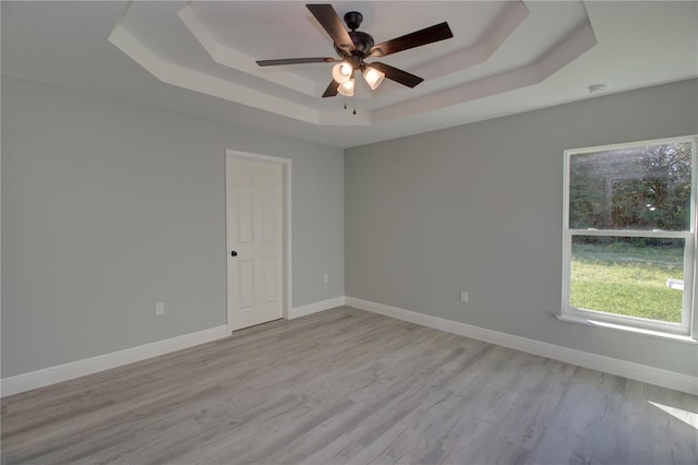 unfurnished room with ceiling fan, a tray ceiling, and light wood-type flooring