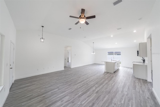 unfurnished living room with visible vents, ceiling fan, vaulted ceiling, wood finished floors, and baseboards