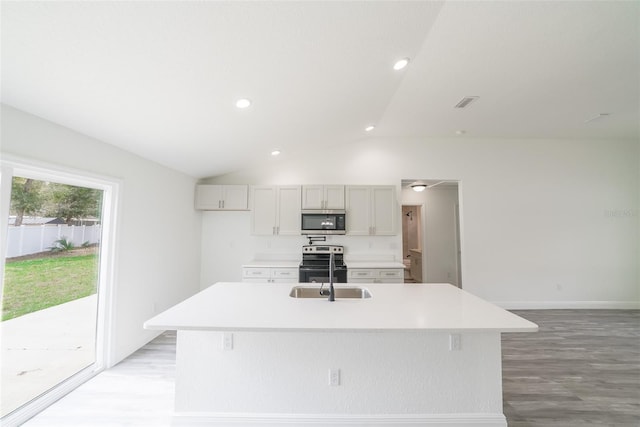 kitchen with a center island with sink, light countertops, light wood-style flooring, appliances with stainless steel finishes, and vaulted ceiling