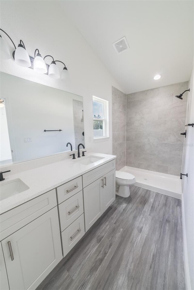 full bathroom featuring visible vents, a sink, a tile shower, and double vanity