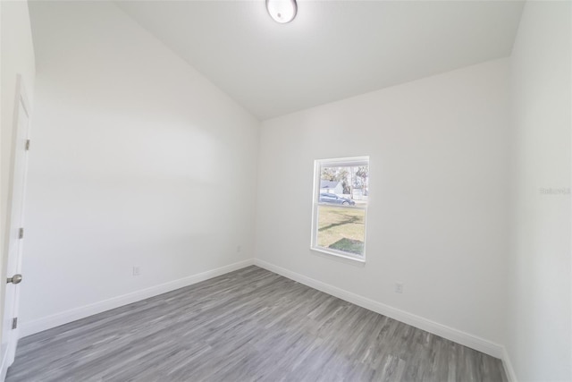 spare room featuring vaulted ceiling, wood finished floors, and baseboards