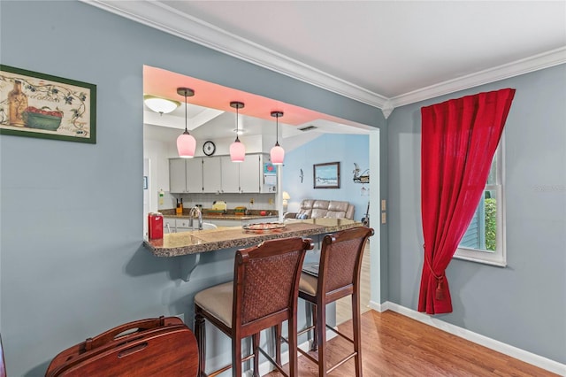 kitchen with kitchen peninsula, pendant lighting, light hardwood / wood-style floors, white cabinets, and ornamental molding