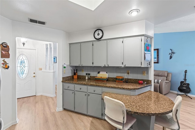 kitchen with kitchen peninsula, a kitchen bar, light wood-type flooring, backsplash, and gray cabinetry