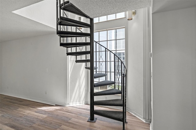 staircase with a textured ceiling, a wealth of natural light, and hardwood / wood-style flooring