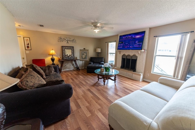 living room with a large fireplace, ceiling fan, hardwood / wood-style flooring, and a textured ceiling