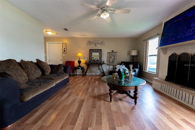 living room with hardwood / wood-style floors, ceiling fan, a fireplace, and a textured ceiling