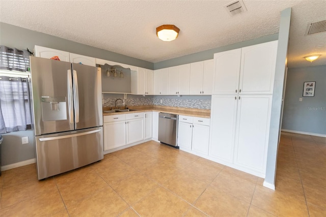 kitchen with appliances with stainless steel finishes, sink, light tile floors, and white cabinets