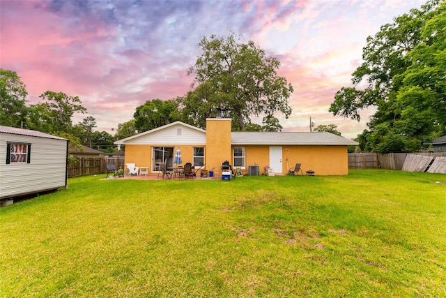 back house at dusk with a patio area, central AC, and a lawn