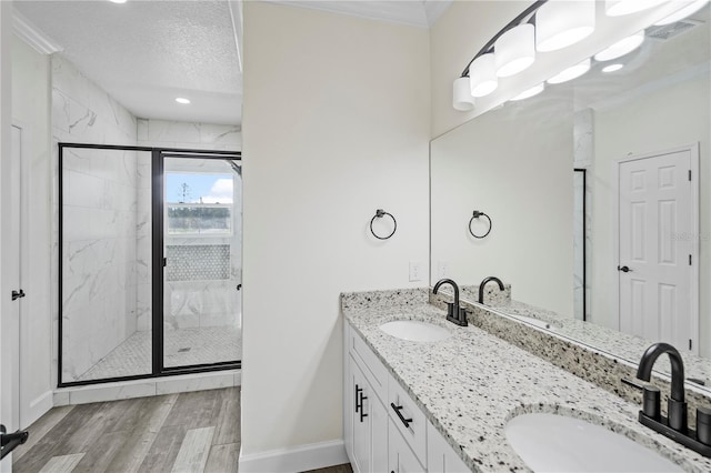 bathroom with a shower with door, vanity, a textured ceiling, and ornamental molding