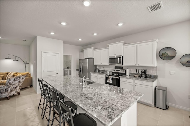 kitchen with a kitchen bar, a large island with sink, white cabinets, and appliances with stainless steel finishes