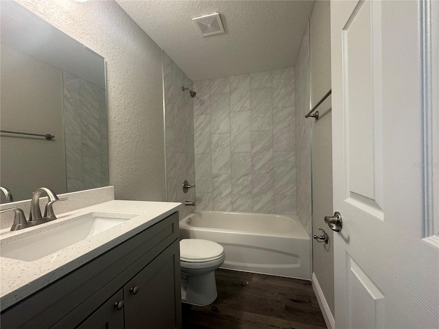 full bathroom featuring tiled shower / bath, wood-type flooring, vanity, toilet, and a textured ceiling