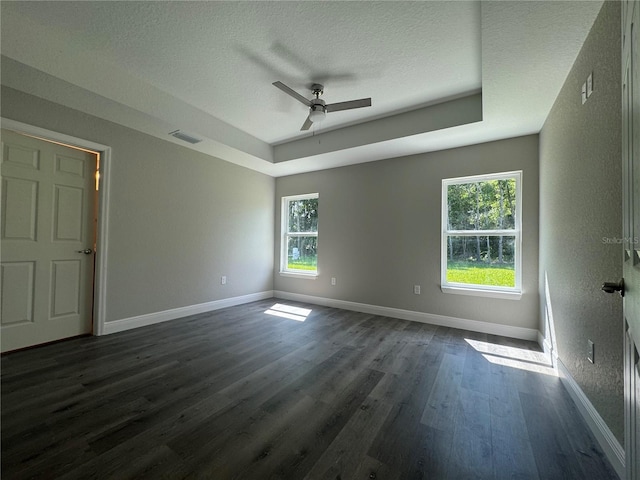 empty room featuring dark wood-type flooring, a textured ceiling, ceiling fan, and a tray ceiling