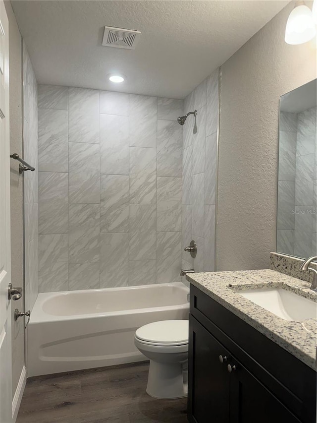 full bathroom with hardwood / wood-style floors, vanity, a textured ceiling, toilet, and tiled shower / bath