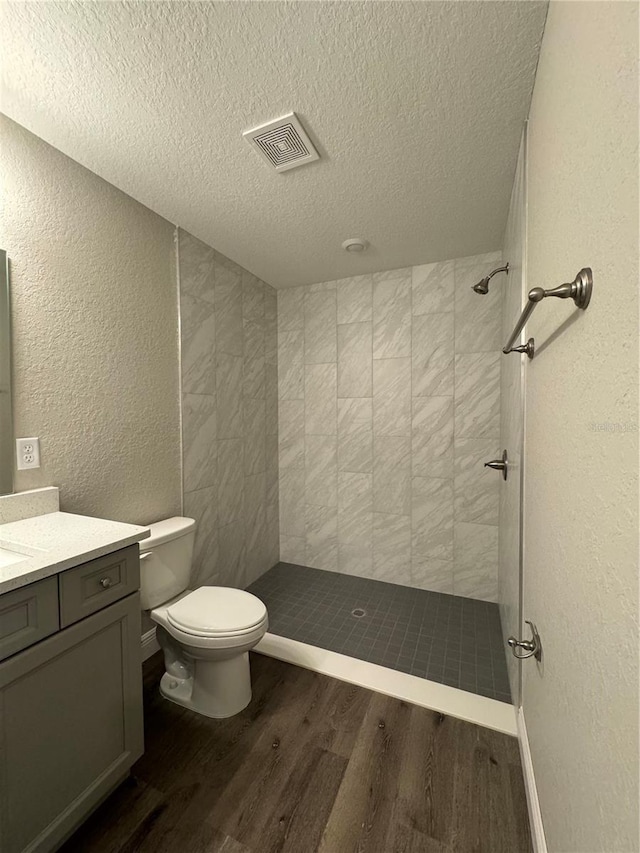 bathroom featuring vanity, a tile shower, hardwood / wood-style floors, and toilet