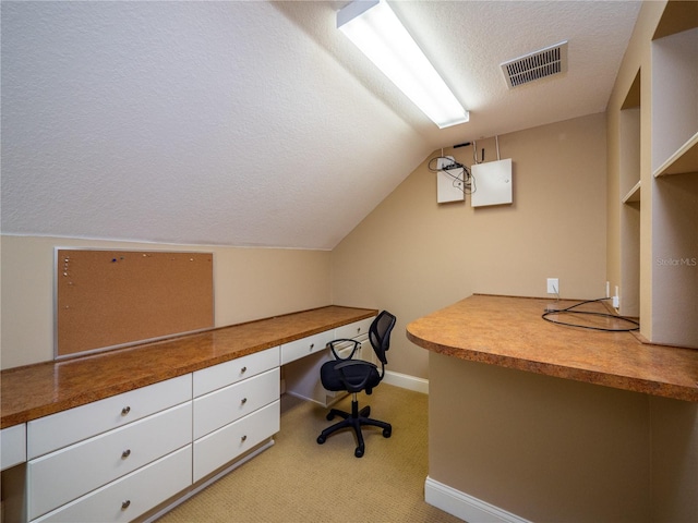 unfurnished office featuring built in desk, lofted ceiling, a textured ceiling, and light colored carpet